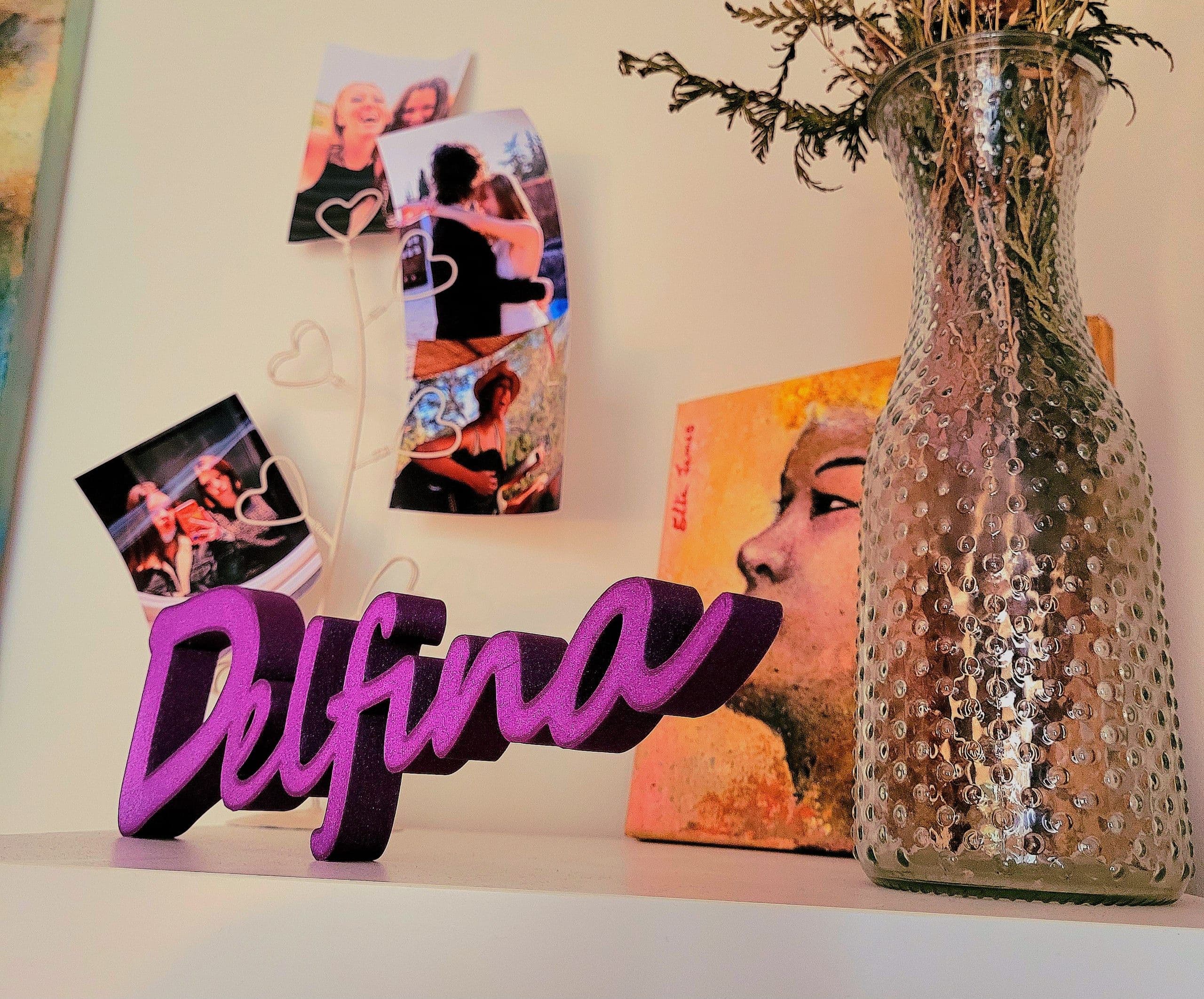 Letras tridimensionales con el nombre Delfina en morado, sobre una repisa