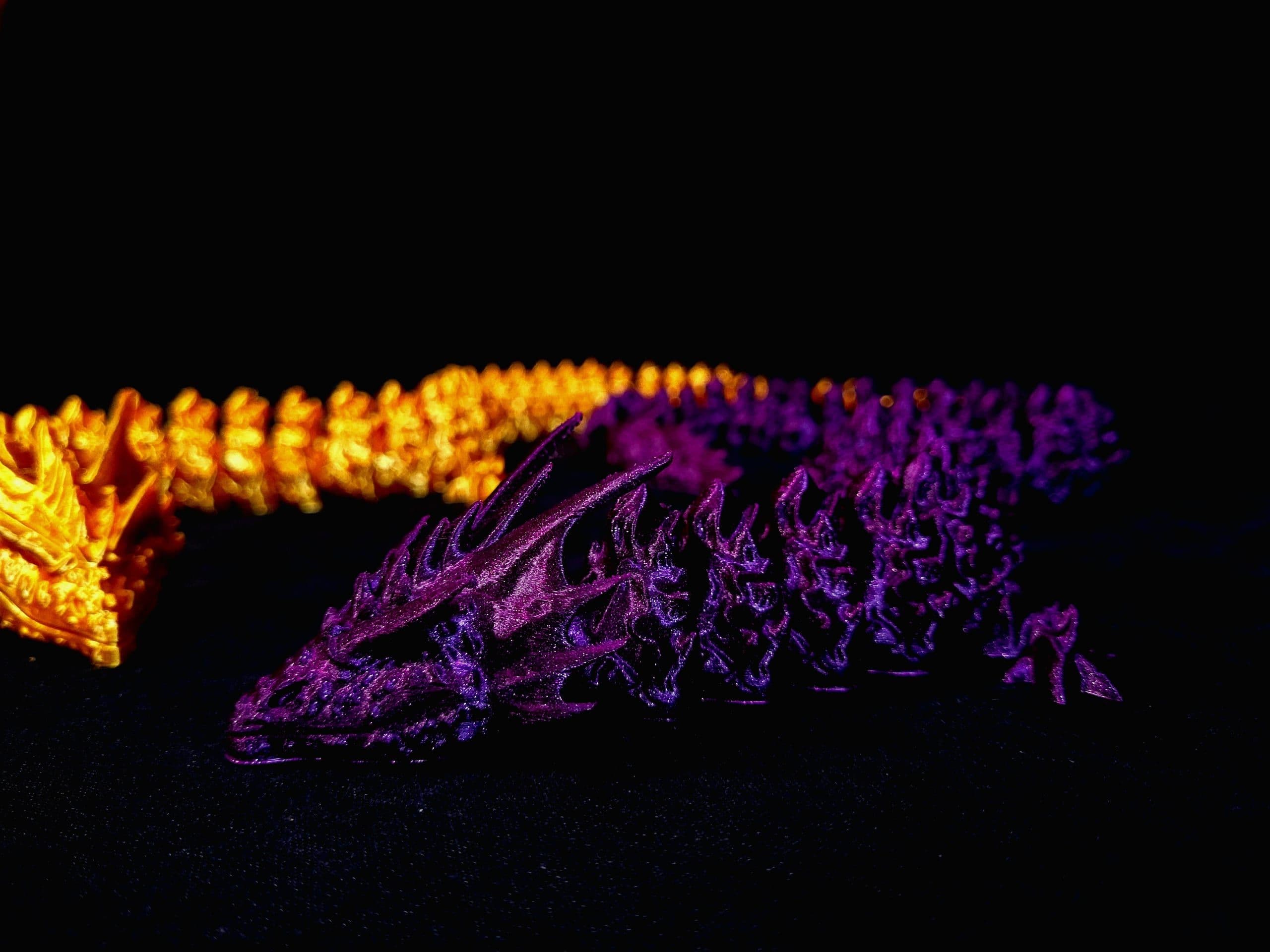 Dos dragones articulados impresos en 3D, uno naranja y otro morado iridiscente, sobre fondo negro