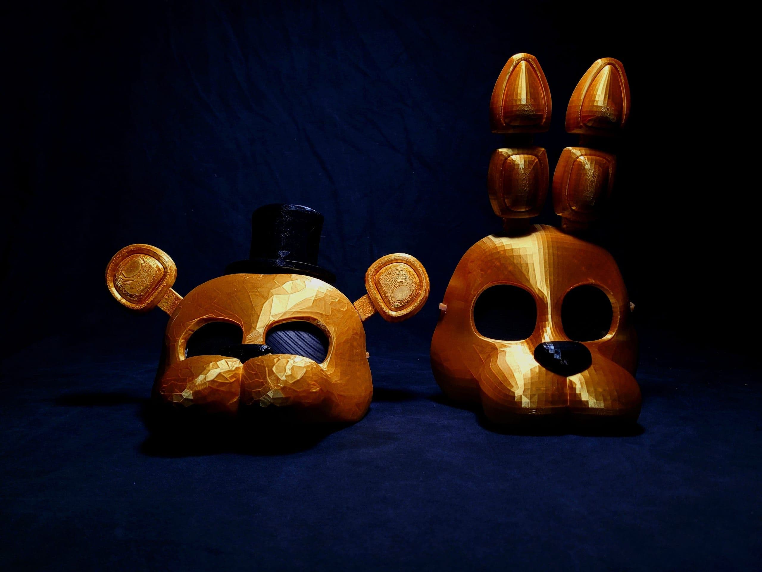 Dos máscaras de gran formato con acabado dorado, una de oso con chistera y otra de conejo