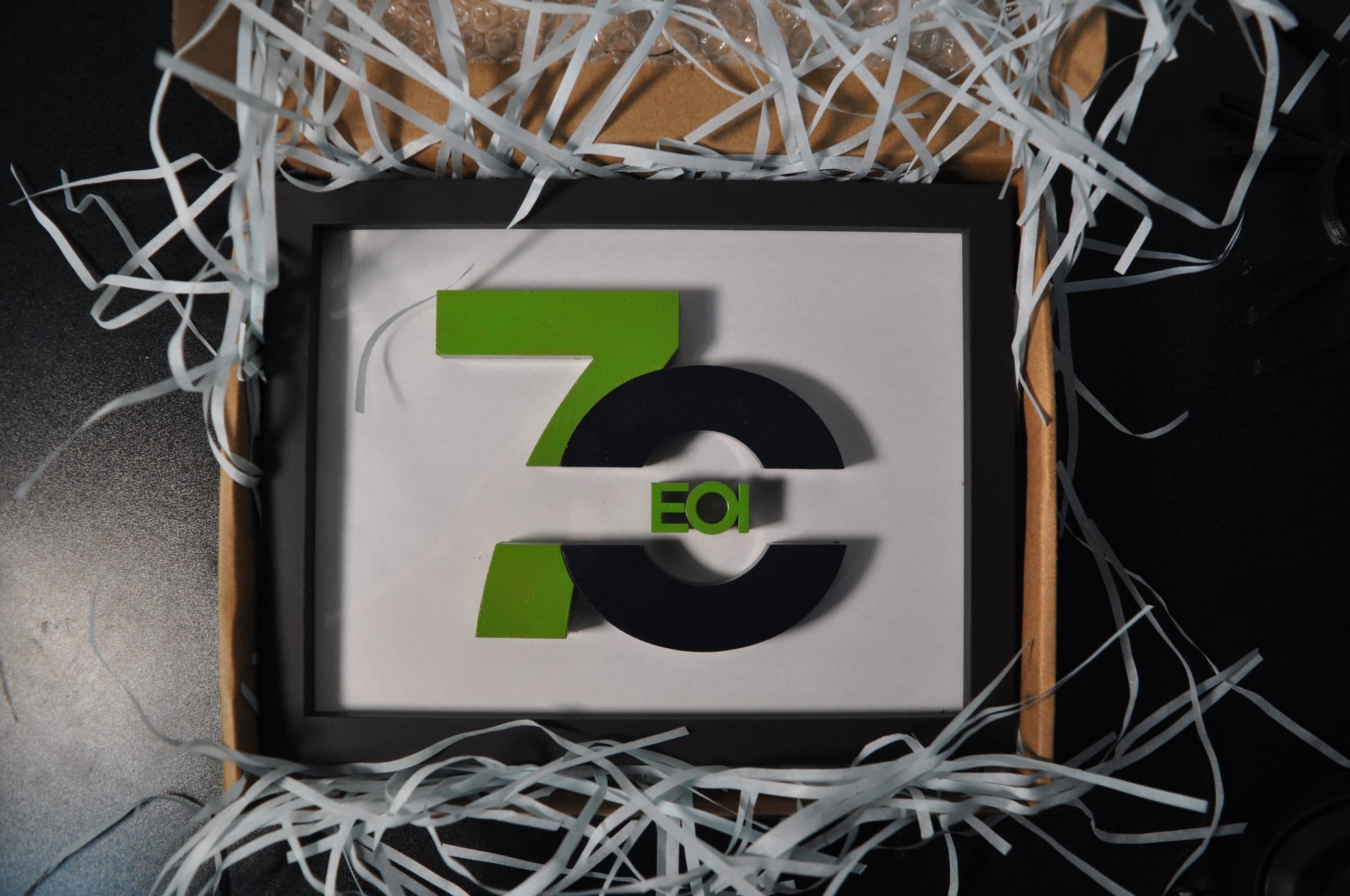 Placa enmarcada con el número 70 de EOI en verde y negro, entre viruta de embalaje blanca